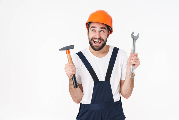 Image of screaming happy young man builder in helmet posing isolated over white wall background holding equipment. - Φωτογραφία, εικόνα
