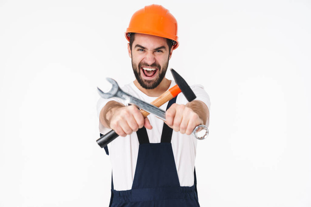 Image of screaming young man builder in helmet posing isolated over white wall background holding equipment. - Фото, зображення