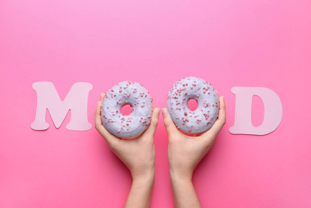 Female hands with tasty doughnuts and word MOOD on color background - Fotó, kép