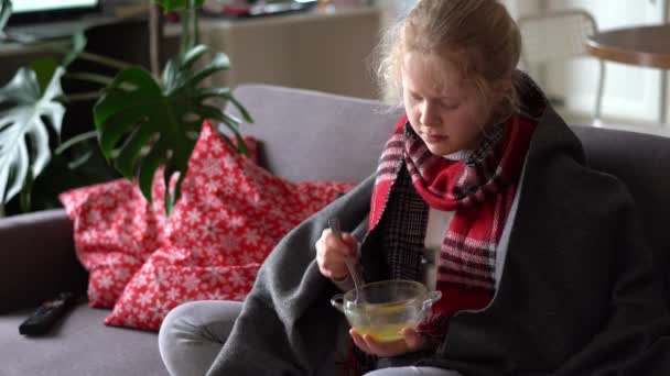 portrait of a sick child in a scarf and plaid, girl eating broth on the sofa in the apartment - Footage, Video