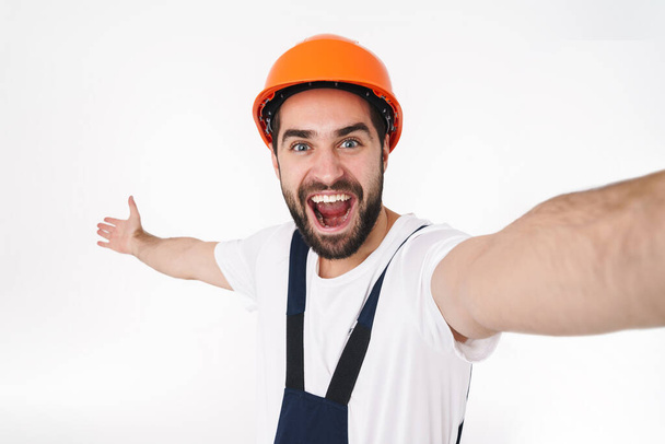 Image of cheery young man builder in helmet isolated over white wall background take selfie by camera. - Фото, зображення
