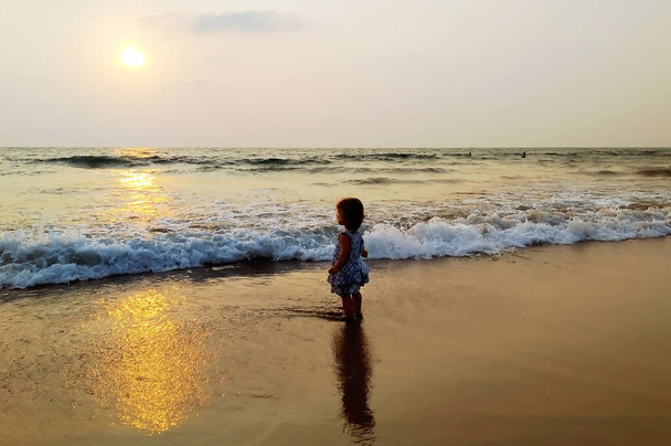 Tyttö seisoo meressä auringonlaskun aikaan, aallot juoksevat pitkin rantaa. Auringon häikäisy ja valon valaistus
. - Valokuva, kuva