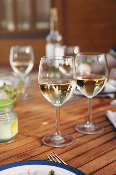 Bahçedeki romantik akşam yemeği sırasında ahşap masaya yerleştirilmiş beyaz şaraplı cam kadehler. - Fotoğraf, Görsel