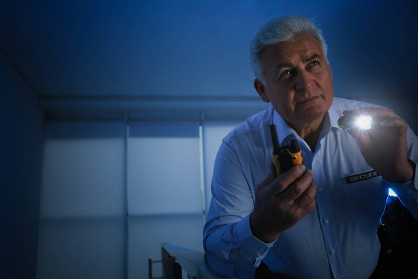 Professional security guard with portable radio set and flashlight in dark room - Фото, изображение