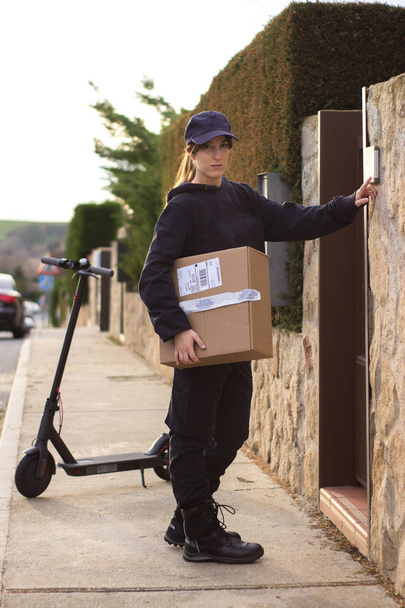 a young messenger in an electric scooter has a cardboard box to deliver in a house - Fotó, kép
