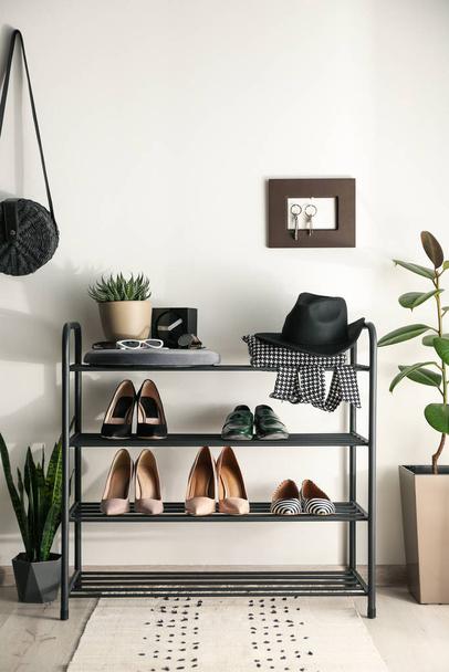 Black shelving unit with shoes and different accessories near white wall in hall - Foto, Bild