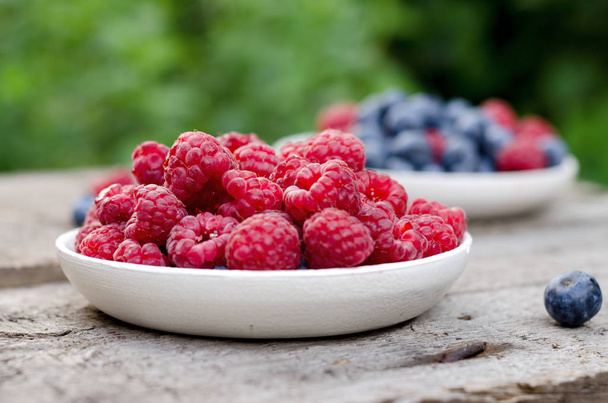 Blueberries and raspberries on an old wooden table, at the garden. Rural natural food style background. - Foto, imagen