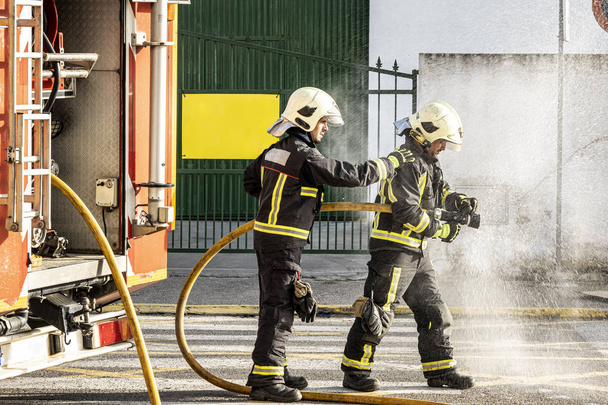 strażacy z wężem wodnym ciągnącym wodę do gaszenia pożaru - Zdjęcie, obraz