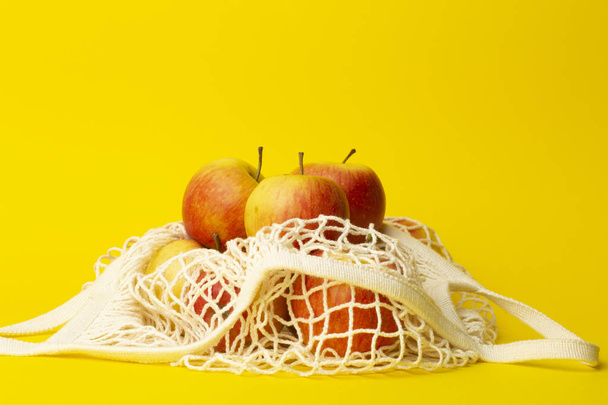 Zero waste concept. Apples in a string bag on a yellow background. No plastic bags in supermarkets and shops concept. - Photo, Image