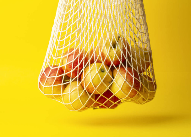 廃棄物ゼロのコンセプト。黄色の背景にストリングバッグにアップル。スーパーマーケットやお店のコンセプトではないビニール袋. - 写真・画像