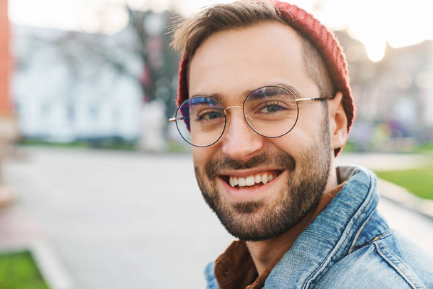 Close up of a handsome happy young stylish bearded man walking outdoors in the street, looking at camera - Fotoğraf, Görsel