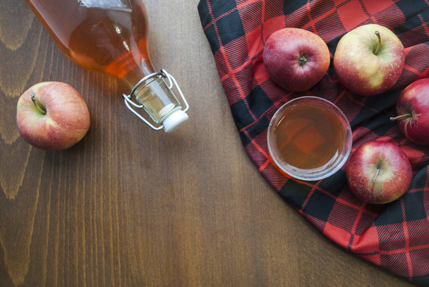 Κάτοψη μπουκαλιού και ποτηριού. Σπιτικό χυμό μήλου. Σε ξύλινο τραπέζι με μαύρο-κόκκινο καρό τραπεζομάντηλο. - Φωτογραφία, εικόνα