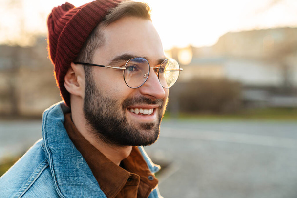 Close up of a handsome happy young stylish bearded man walking outdoors in the street, looking away - Foto, Imagen