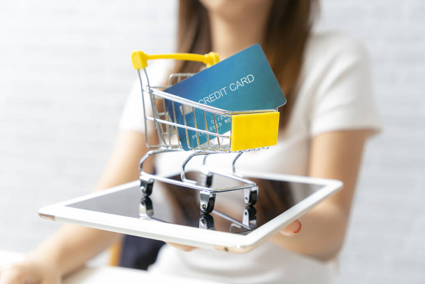 A bevásárlókosarat tartó üzletasszonyok bankkártyát tartalmaznak tablettán. - Fotó, kép