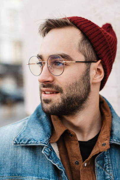 Close up of a handsome young stylish bearded man walking outdoors in the street, looking away - Foto, Bild
