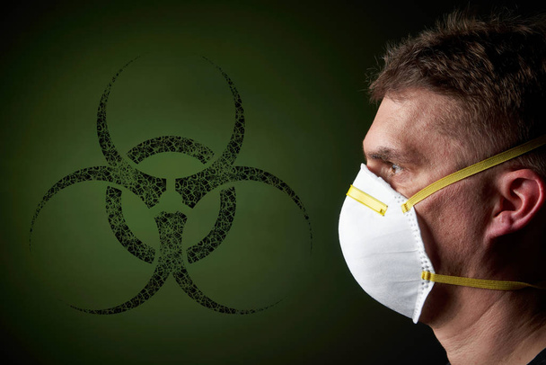 side view / profile of a young man wearing a protective mask in dark atmosphere - black biohazard sign / emblem on green background - Foto, Bild