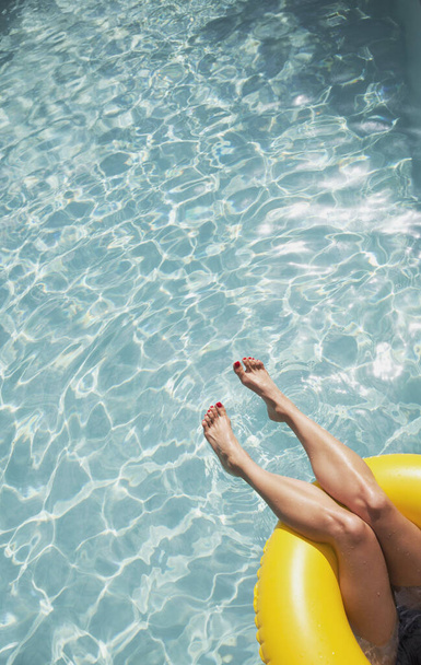 素足でリラックスした女性,日当たりの良いスイミングプールでインフレータブルリングに浮かんで - 写真・画像