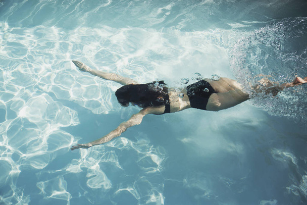Γυναίκα με μπικίνι που κολυμπάει κάτω από το νερό στην ηλιόλουστη πισίνα - Φωτογραφία, εικόνα