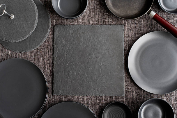 piles of black ceramic dishes and tableware top view on gray background - Fotó, kép