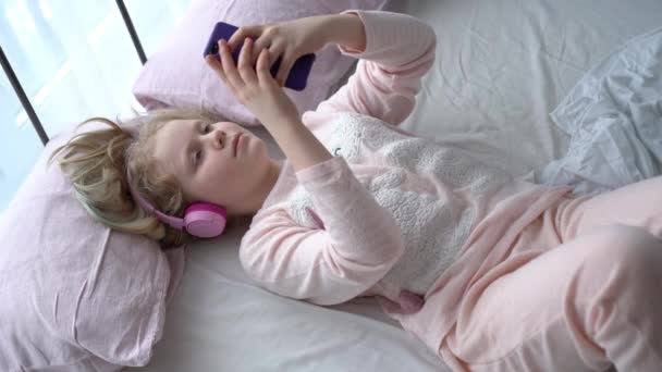 moderní život generace Z. dospívající dívka v pyžamu a sluchátka v místnosti na posteli poslouchá hudbu z chytrého telefonu. - Záběry, video