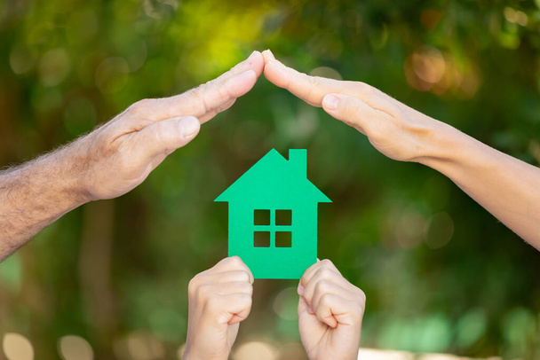 Family holding house in hands against spring green background. Real estate and healthy lifestyle concept - Foto, Imagem