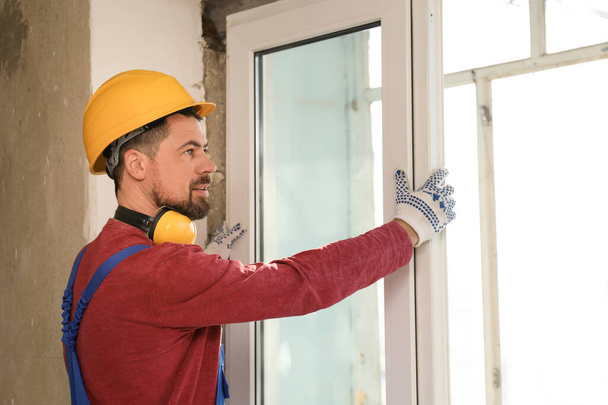 Worker in uniform installing plastic window indoors - Фото, зображення