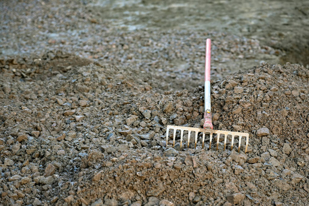 Металлические грабли лежат на груде гравия на строительной площадке
 - Фото, изображение