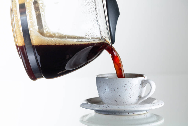 Fekete kávé egy kerámia pohárban egy üvegasztalon. A kávét a kávéfőzőből egy pohárba öntik. Fénymásolási hely. - Fotó, kép