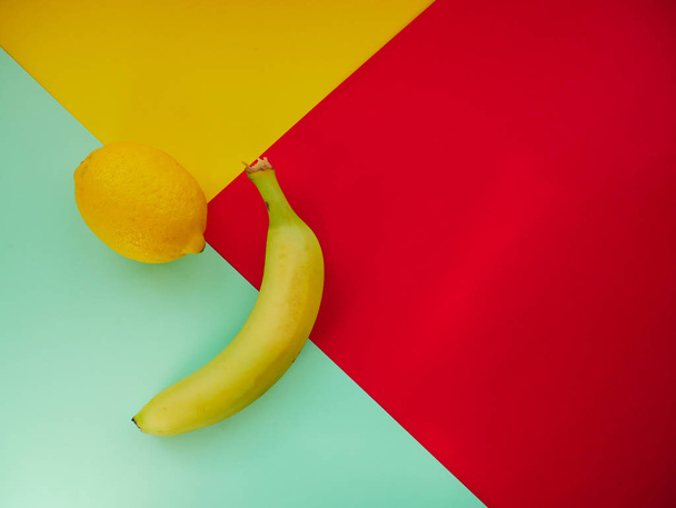 色の背景にレモンとバナナ、トップビュー。トレンディカラフルな写真。カラフルな紙の背景と最小限のスタイル。フラットレイファッションコンセプト:パステルを背景にレモンとバナナ. - 写真・画像