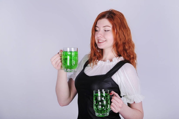 Гарна жінка в сукні з склянками зеленого пива, що позують на сірому фоні. З Днем святого Патрика. - Фото, зображення