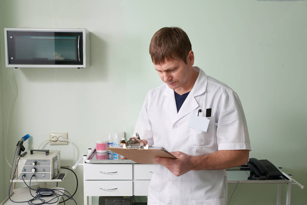 lekarz stojący w swoim laboratorium, trzymający notatnik i piszący diagnozę - Zdjęcie, obraz
