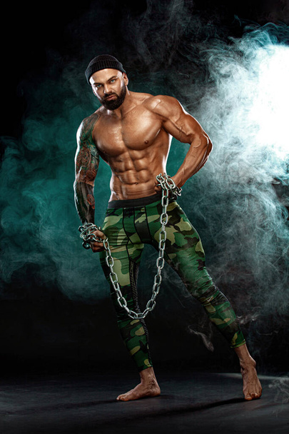 Athlete bodybuilder on black background with lights and smoke. Men fashion. Portrait of a brutal bearded man topless with chains. - Fotografie, Obrázek