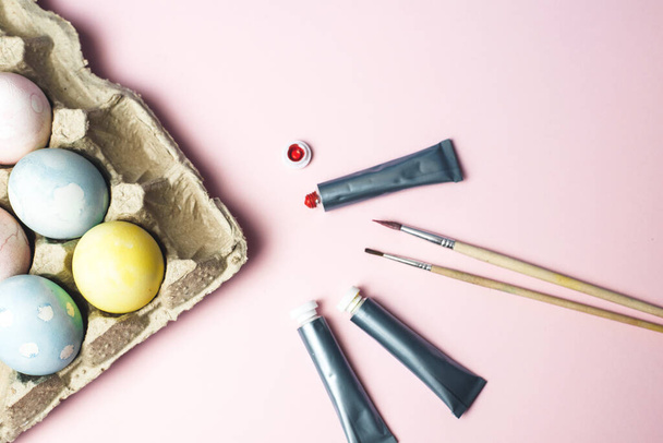 El concepto de colorear huevos de Pascua en colores pastel acuarela. Pinturas y pinceles para colorear huevos para Pascua sobre fondo rosa
. - Foto, imagen