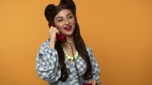 Smiling pin up woman looking around and talking on retro telephone - Video