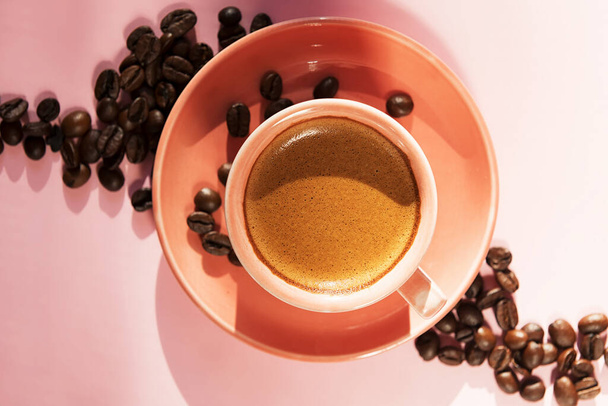コーラル色のカップにコーヒー豆を使用し、パステルローズの背景に影をつけています。平置きだ。最上階だ。ミニマリスト、コーヒーコンセプト。夏の静物 - 写真・画像