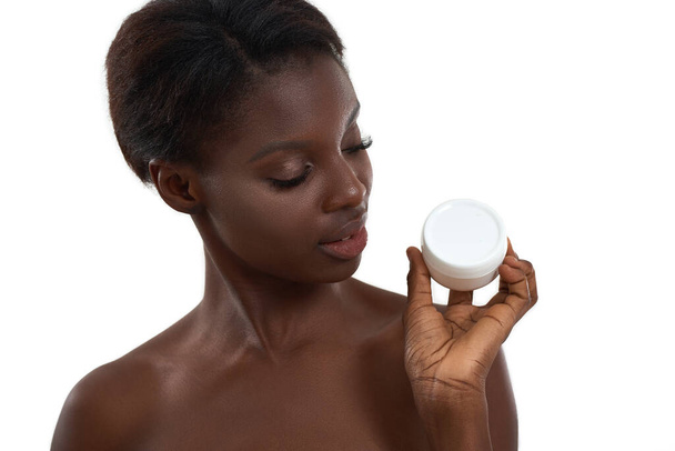 Testing daily cream. Portrait of beautiful young african woman demonstrating cosmetic product and looking at camera while standing in studio against white background - Fotografie, Obrázek
