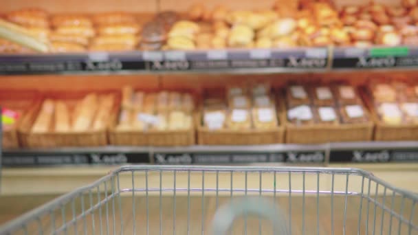 Metalowy wózek na żywność porusza się i stoi w supermarkecie, wśród półek z towarami - Materiał filmowy, wideo