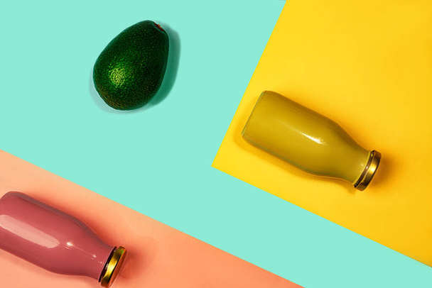 Bottles of multicolored juices or smoothies and avocado on yellow, pink coral and trendy mint green blue background. - Фото, изображение