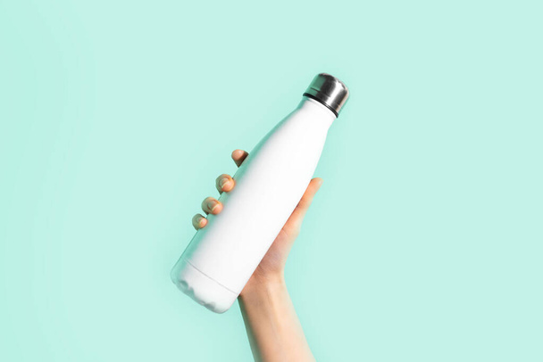 Close-up of female hand, holding white reusable steel stainless eco thermo water bottle with mockup, isolated on background of cyan, aqua menthe color. Be plastic free. Zero waste. - Foto, imagen