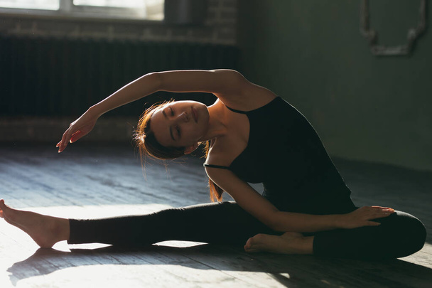 Girl in black sportswear doing yoga on the floor in the gym. - Fotoğraf, Görsel