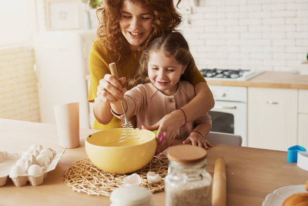Mutter und Tochter bereiten gemeinsam in der Küche einen Kuchen zu - Foto, Bild