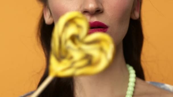 Oříznutý pohled na brunetky dívka lízání candy a usmívání na žlutém pozadí - Záběry, video