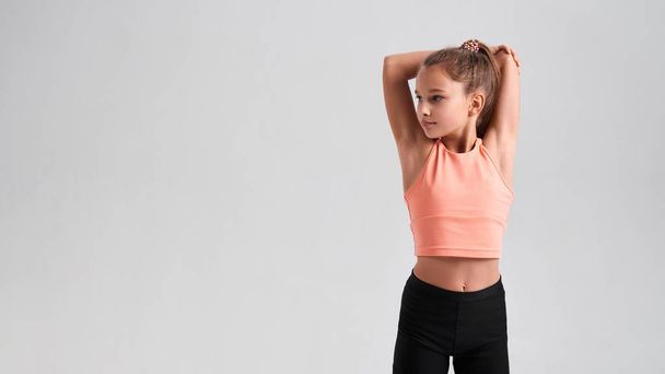 Stay healthy. Flexible cute little girl child looking aside while stretching her body isolated on a grey background. Sport, training, fitness, active lifestyle concept. Horizontal shot. - Foto, Imagem