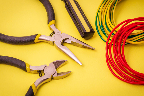New electrician tools and wires on a yellow background for repairing energized systems or communications - Φωτογραφία, εικόνα
