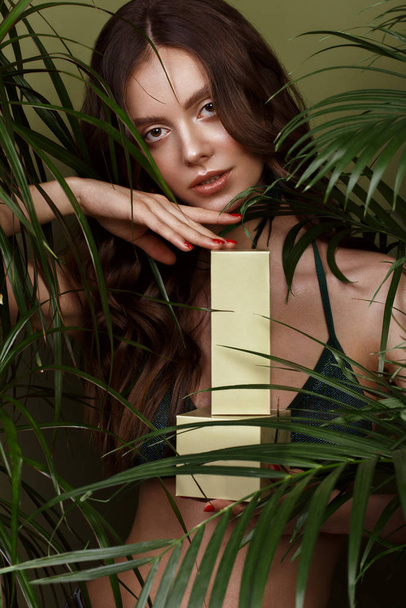 Beautiful sexy woman in a bikini posing in the middle of green plants with a box of cosmetics in hand. Summer look. Beauty face - Valokuva, kuva