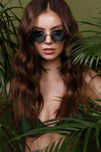 Beautiful sexy woman in a bikini posing in the middle of green plants. Summer look. Beauty face - Photo, Image