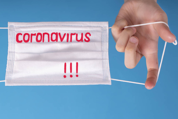 Chinese uitbraak van het coronavirus. Handen op een blauwe achtergrond met een beschermmasker met de tekst Coronavirus.Coronovirus Quarantaine Concept. - Foto, afbeelding