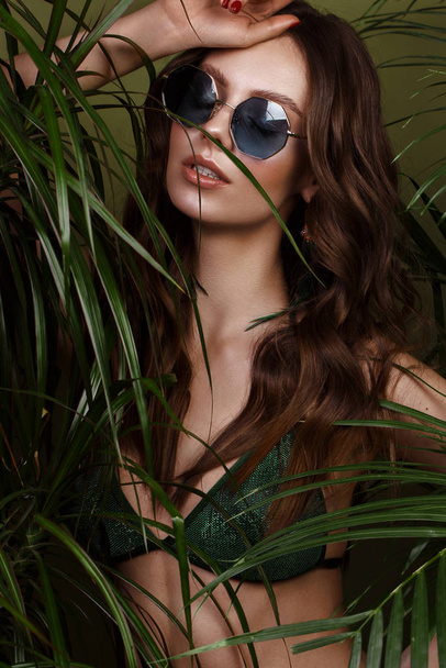 Beautiful sexy woman in a bikini posing in the middle of green plants. Summer look. Beauty face - Foto, Imagen