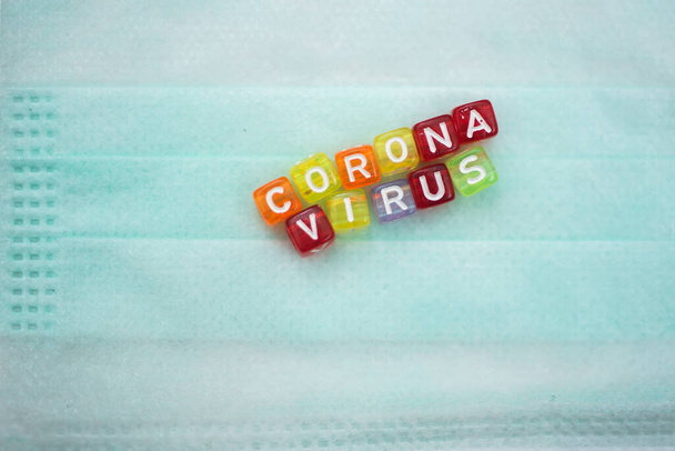 Colorful word CORONA VIRUS english alphabet cube on face mask, selective focus - 写真・画像