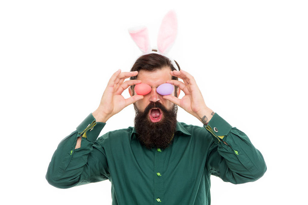 春休みのお祝い。文化習慣や伝統。イースターバニー色の卵。ウサギの耳とイースターエッグを持つ髭の男。イースターグッズを探しています。長い耳を持つヒップスター卵を保持 - 写真・画像